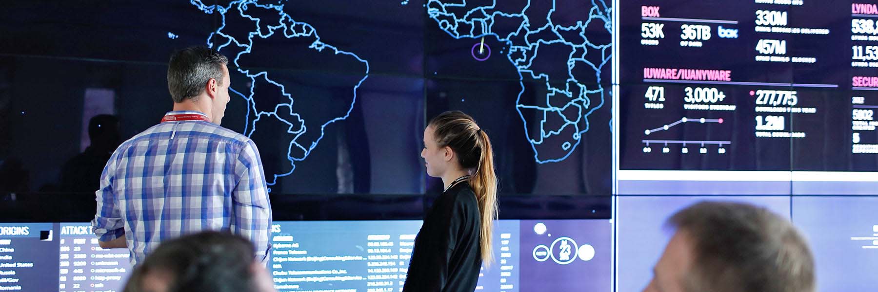 An employee shows a student a map and security data on screens in the Cyberinfrastructure Building.