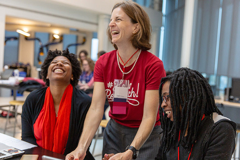 A faculty researcher laughs as she works on a research project with two students at a workshop.