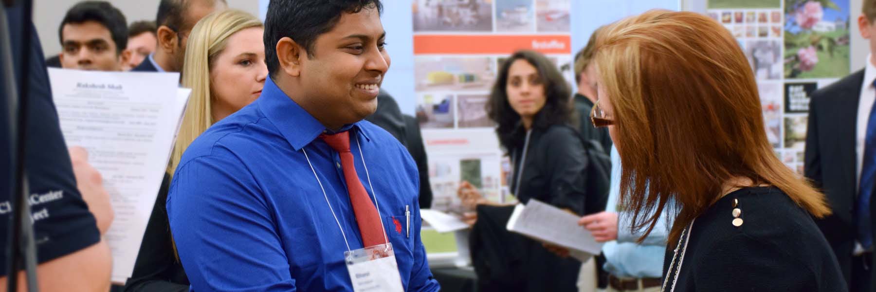 A student smiles at a company representative at a career fair.