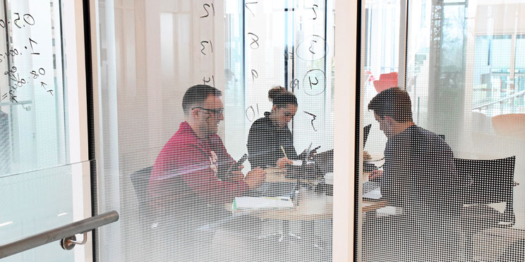 A female and two males studying inside an all glass study area inside of Luddy Hall