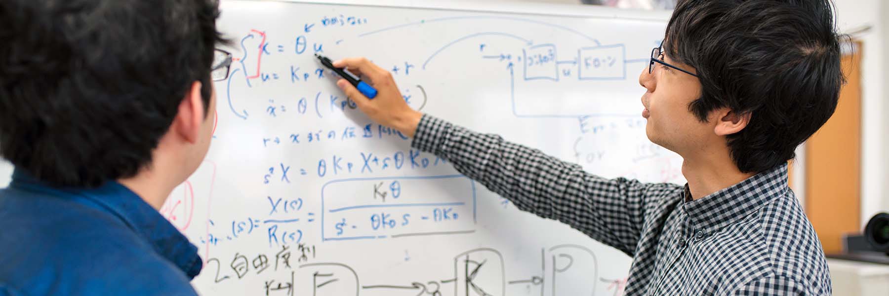 Two students work on an equation on a whiteboard.